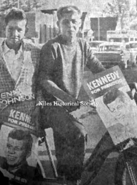 Merle Fick (on bicycle seat) and an unidentified friend display their Kennedy posters as they pose for a picture where Haydu’s gas station now stands at the intersection of Robbins Avenue and North Main Street.