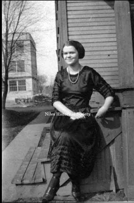 Violet Stein McGuirk sitting on the back porch of her parent's house at the corner of East Madison and John Street, in the summer of 1921. In the background is the remaining construction material for the Roosevelt School that opened in 1921. Later, this school would become the high school annex.