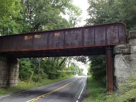 The steel girder railroad bridge that overpasses the roadway.