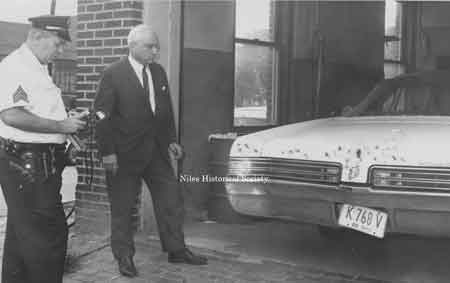 Patrolman John Scott and police Chief Ross inspect a bullet-ridden car that tried to evade capture. 1969.
