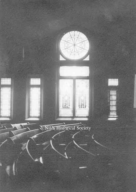 A photo of the interior of the old First Presbyterian Church located on the corner of Main and Church Streets. The rose window from the inside and curved seats.