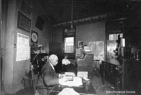 February 1917, Allie Taylor in background with George Taylor, at Home Federal Savings Bank located in the Hartzell Building, built 1889, corner of Main and State Streets, Niles, Ohio.